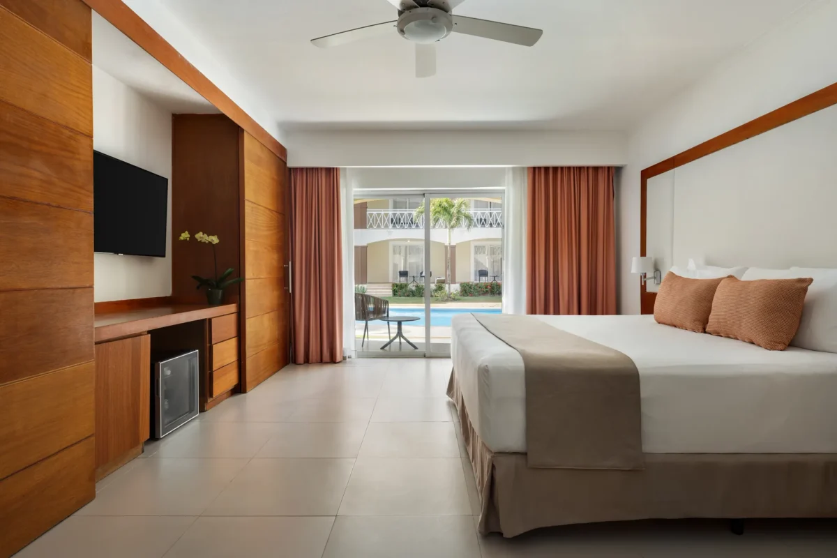 Sun Club Deluxe Junior Suite with king-size bed and balcony overlooking the pool at Sunscape Coco Punta Cana.