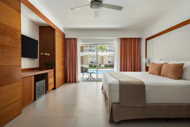 Sun Club Deluxe Junior Suite with king-size bed and balcony overlooking the pool at Sunscape Coco Punta Cana.
