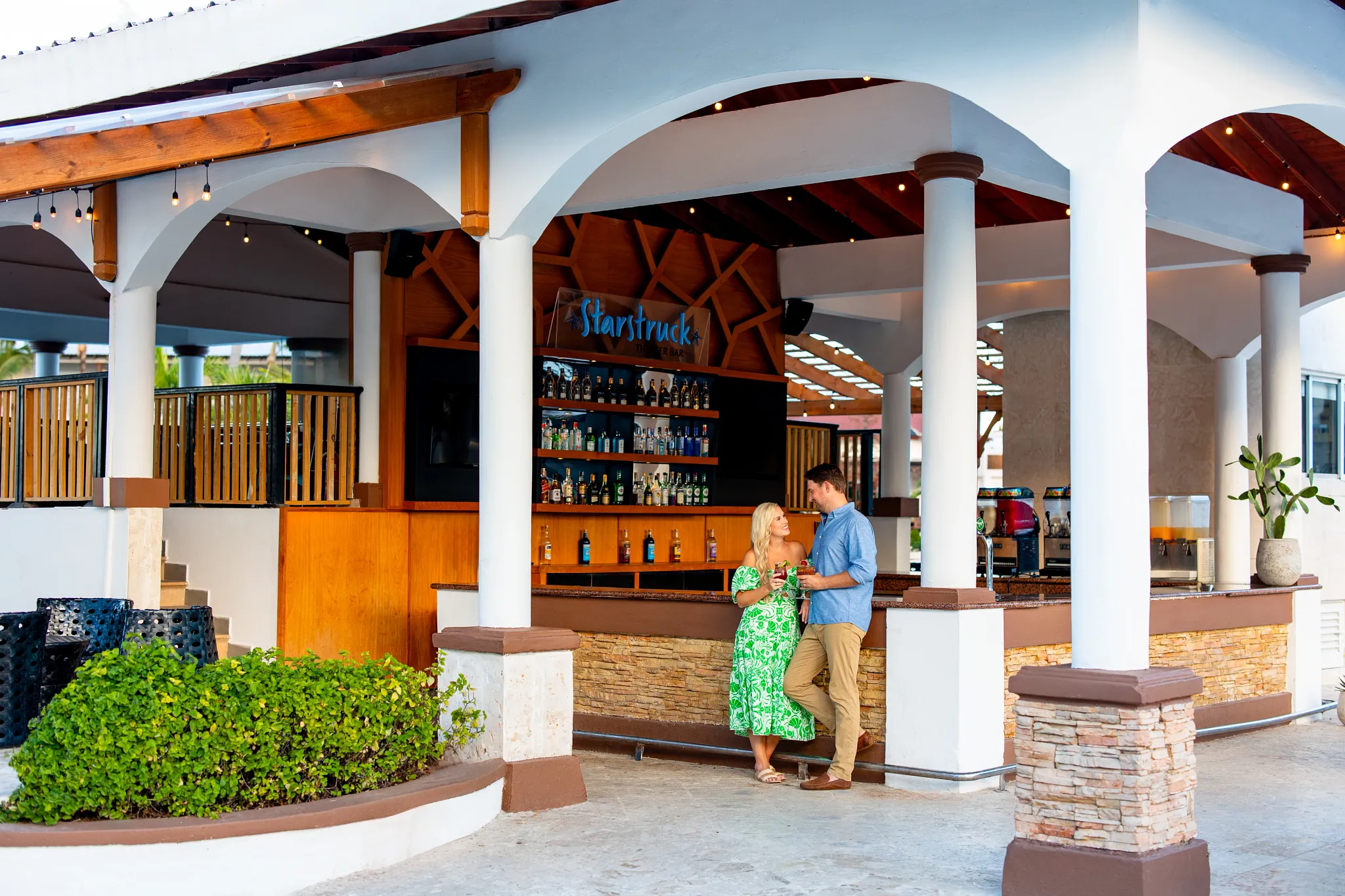 Couple enjoying tropical cocktails at an open-air resort bar at Sunscape Coco Punta Cana in the Dominican Republic.