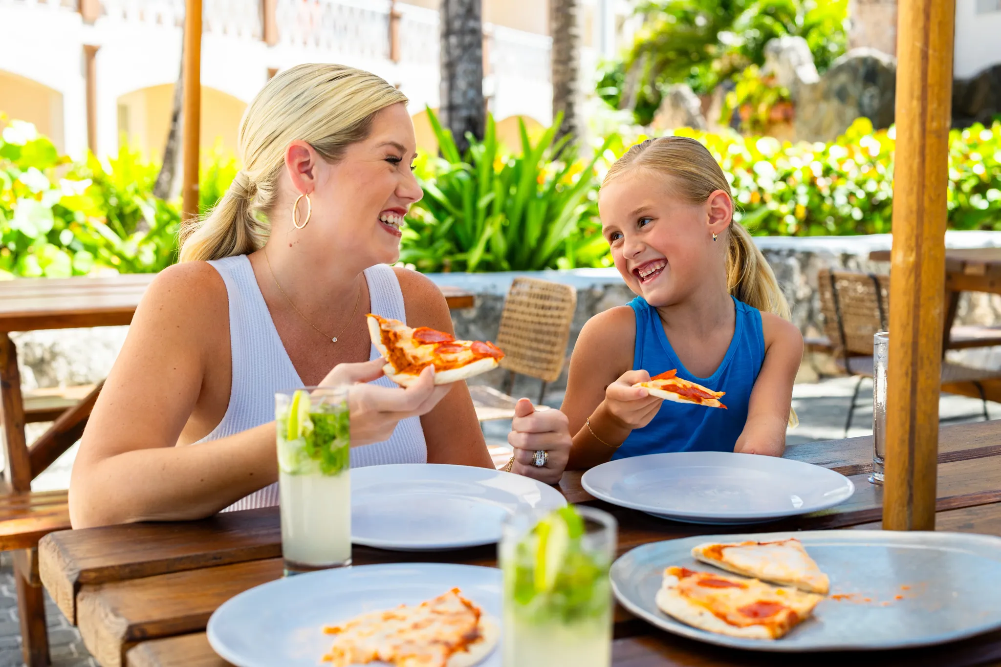 Mother and daughter sharing pizza and drinks at an outdoor restaurant at Sunscape Coco Punta Cana Resort.