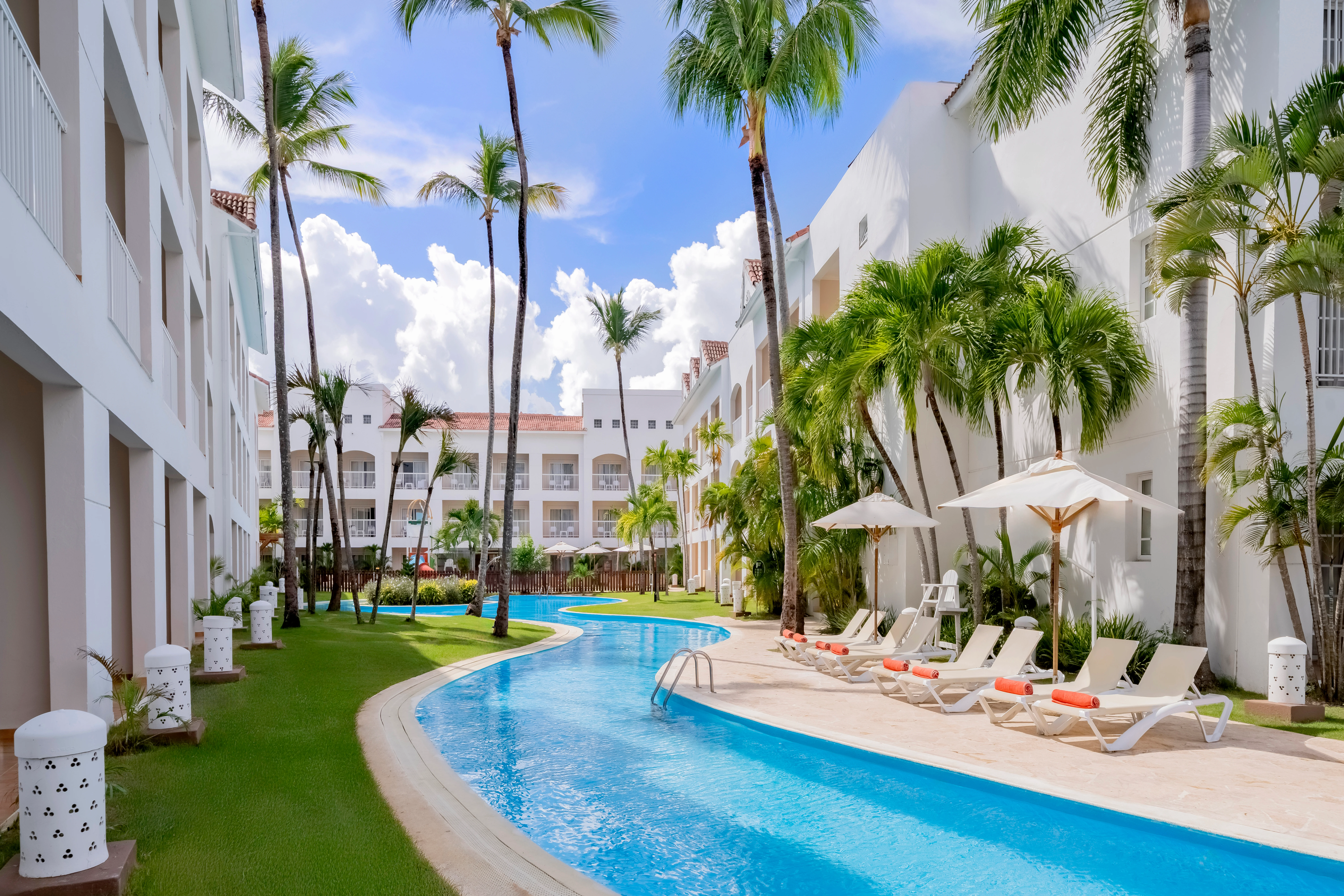 Relaxing pool area lined with palm trees and lounge chairs at Sunscape Coco Punta Cana Resort.