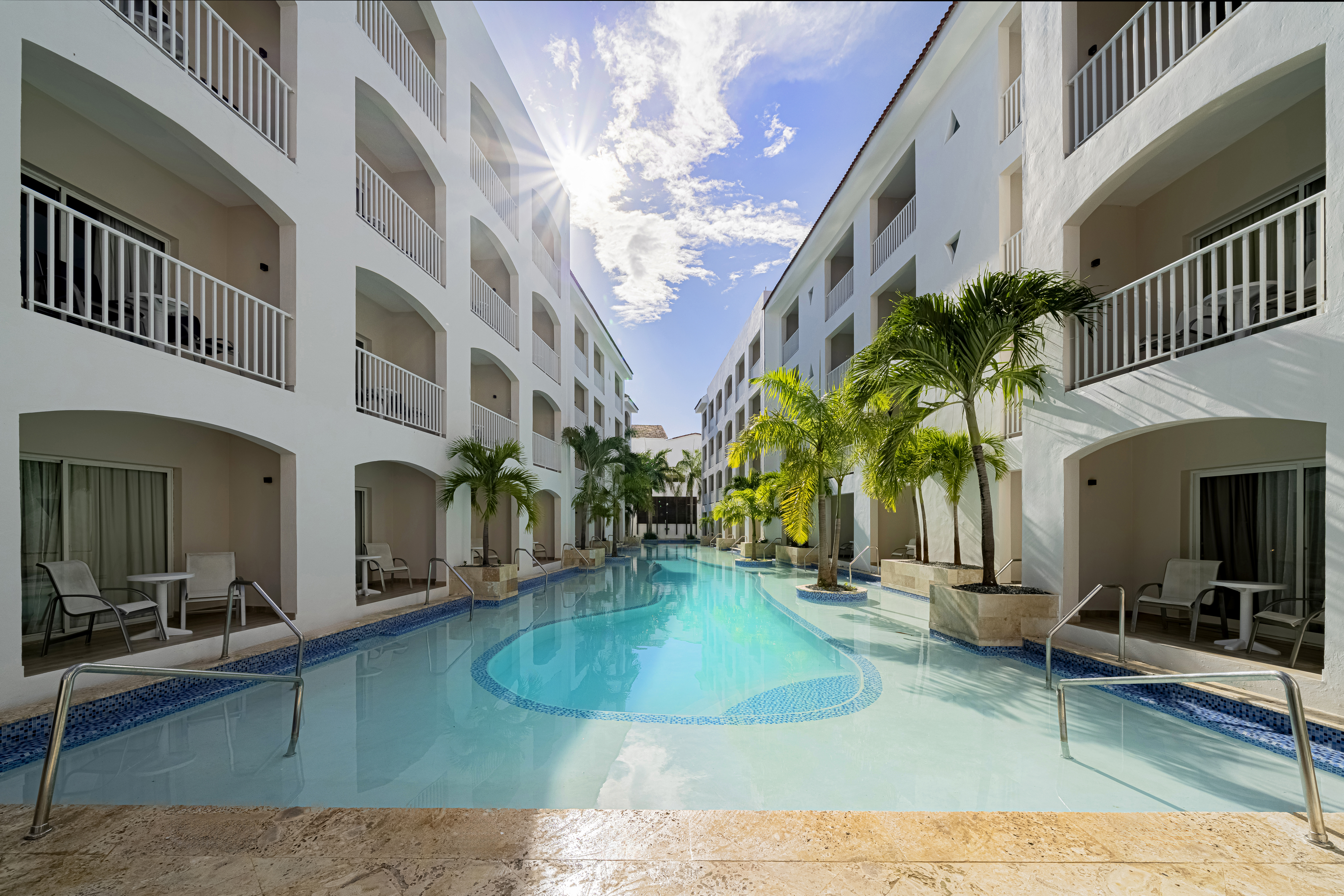 Swim-out pool surrounded by guest rooms and palm trees at Sunscape Coco Punta Cana Resort.